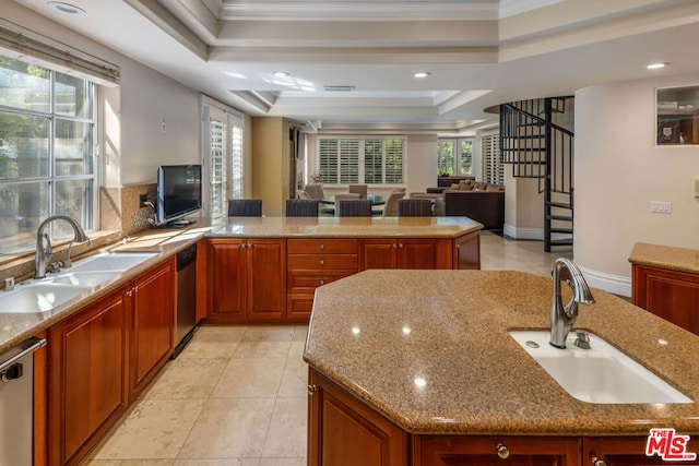 kitchen with crown molding, a tray ceiling, sink, and an island with sink