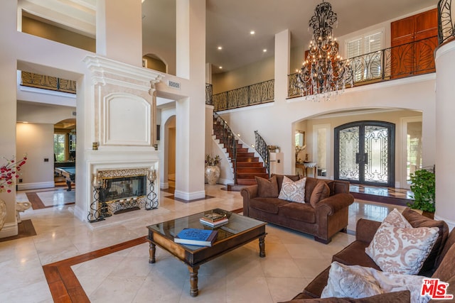 living room with light tile patterned floors, a high end fireplace, a high ceiling, french doors, and a notable chandelier