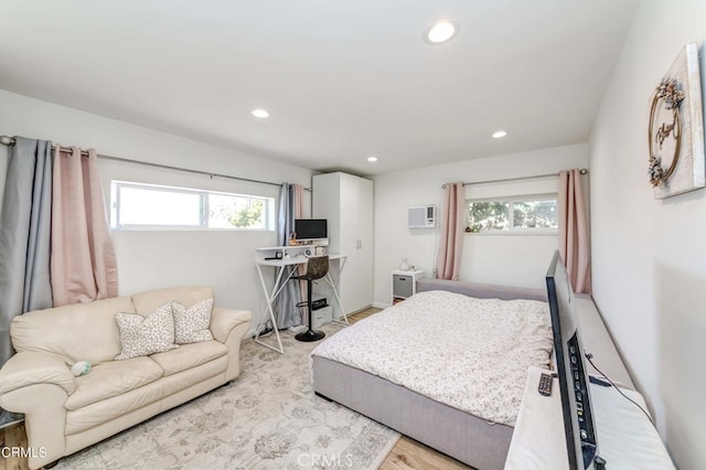 bedroom featuring a wall unit AC, multiple windows, and light wood-type flooring