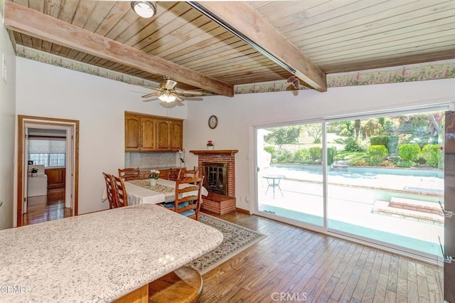 dining space featuring a brick fireplace, ceiling fan, light wood-type flooring, beamed ceiling, and wood ceiling