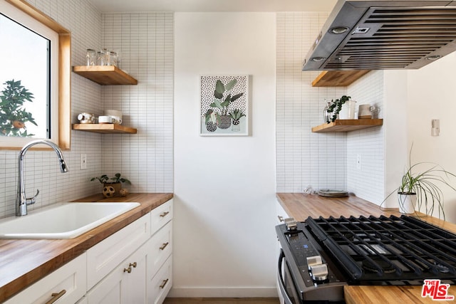 kitchen featuring white cabinetry, backsplash, range hood, wood counters, and sink