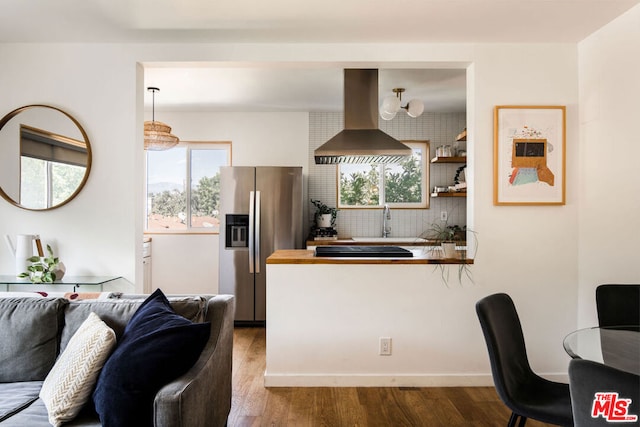 kitchen featuring hanging light fixtures, decorative backsplash, range hood, stainless steel refrigerator with ice dispenser, and hardwood / wood-style floors