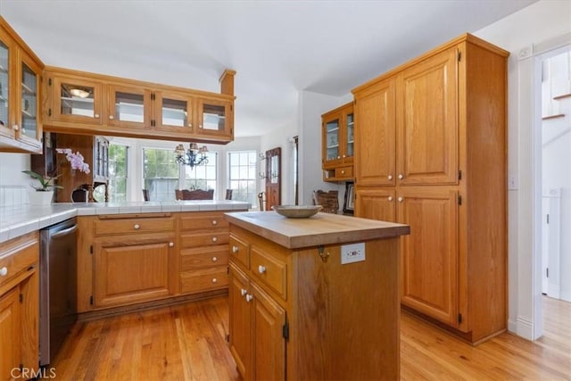 kitchen with dishwasher, a center island, an inviting chandelier, tile countertops, and light hardwood / wood-style flooring