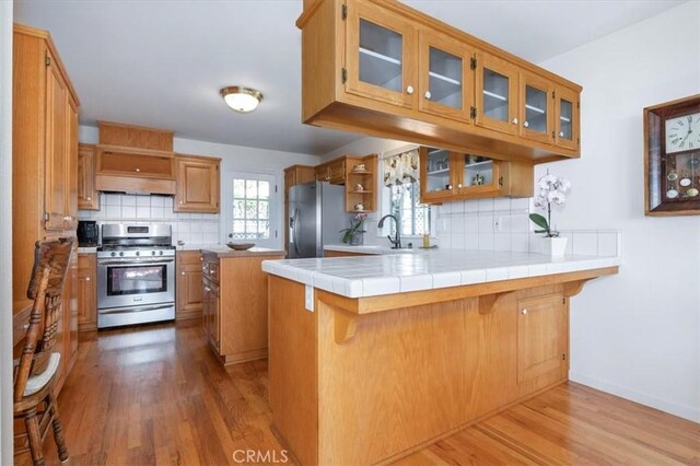 kitchen with tile counters, appliances with stainless steel finishes, kitchen peninsula, and a breakfast bar area