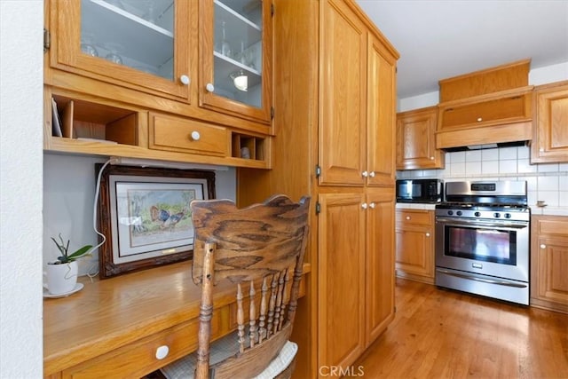 kitchen with custom exhaust hood, hardwood / wood-style floors, stainless steel gas range oven, and decorative backsplash