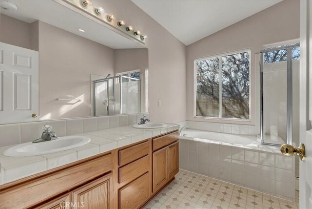 bathroom featuring vanity, vaulted ceiling, and shower with separate bathtub