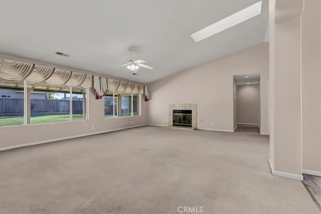 unfurnished living room with ceiling fan, vaulted ceiling with skylight, a fireplace, and light colored carpet