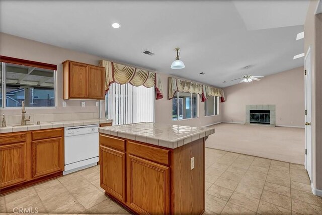 kitchen with a kitchen island, sink, white dishwasher, a tiled fireplace, and tile counters