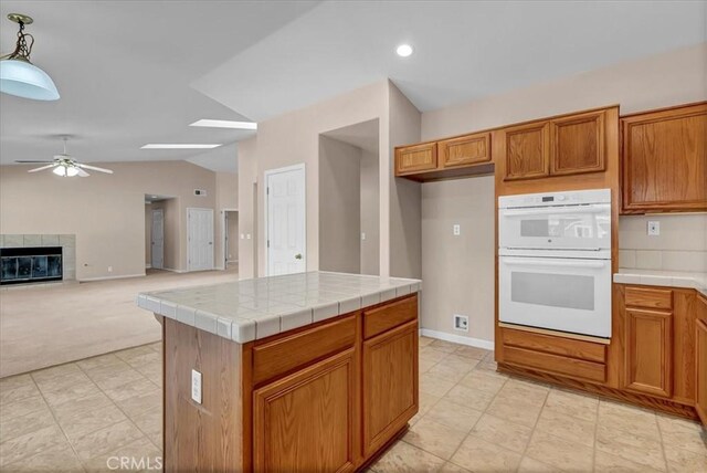 kitchen featuring tile countertops, a fireplace, hanging light fixtures, double oven, and a center island