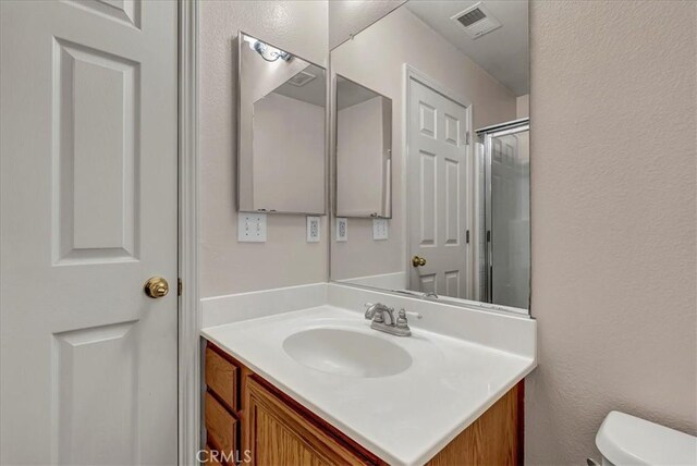 bathroom featuring a shower with door, toilet, and vanity