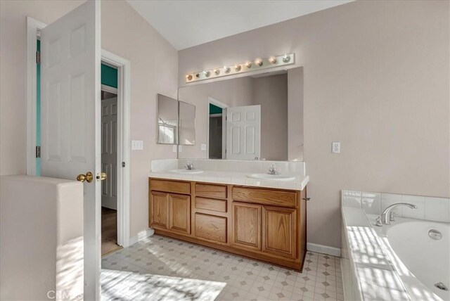 bathroom with lofted ceiling, tiled tub, and vanity