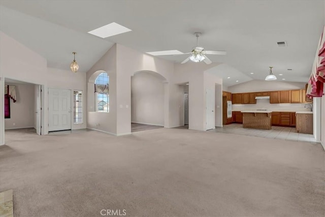 unfurnished living room with ceiling fan, sink, vaulted ceiling with skylight, and light carpet