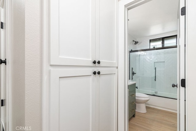 bathroom featuring hardwood / wood-style flooring, toilet, and bath / shower combo with glass door