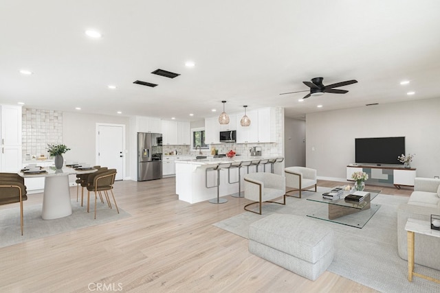 living room featuring ceiling fan, light wood-type flooring, and sink