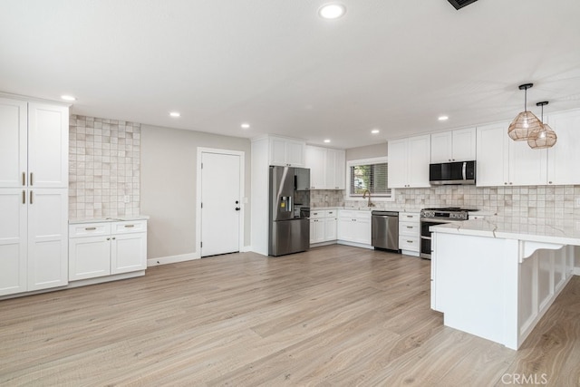 kitchen with appliances with stainless steel finishes, light wood-type flooring, tasteful backsplash, decorative light fixtures, and white cabinetry