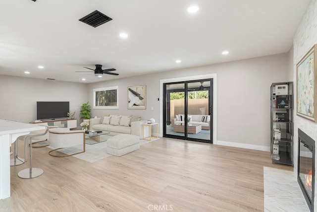 living room with a fireplace, light hardwood / wood-style flooring, and ceiling fan