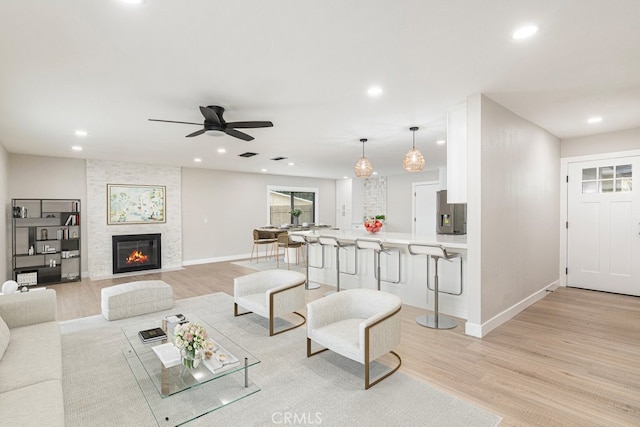 living room with light hardwood / wood-style flooring, ceiling fan, and a stone fireplace