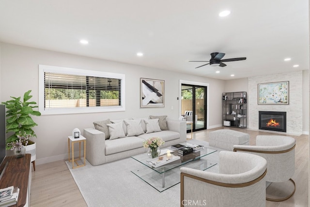 living room featuring ceiling fan, a stone fireplace, and light hardwood / wood-style flooring