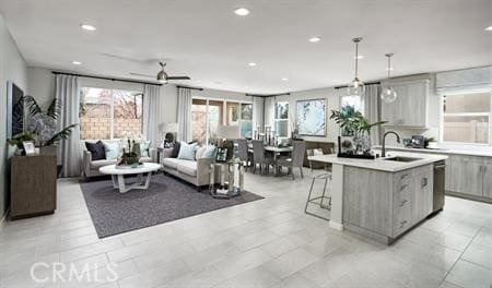 kitchen with gray cabinetry, ceiling fan, sink, hanging light fixtures, and a center island with sink