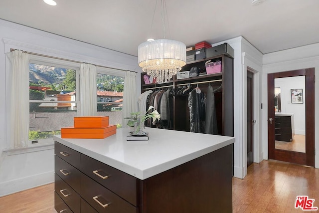 spacious closet with light hardwood / wood-style floors and an inviting chandelier