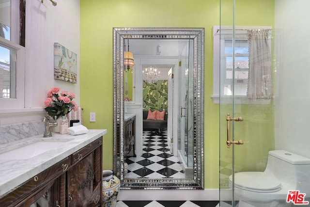 bathroom featuring a notable chandelier, vanity, a shower with shower door, and toilet