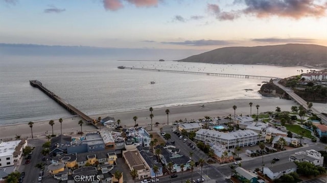 aerial view at dusk with a water and mountain view and a view of the beach