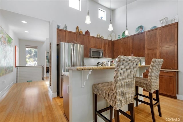 kitchen featuring appliances with stainless steel finishes, decorative light fixtures, a kitchen bar, and light hardwood / wood-style floors