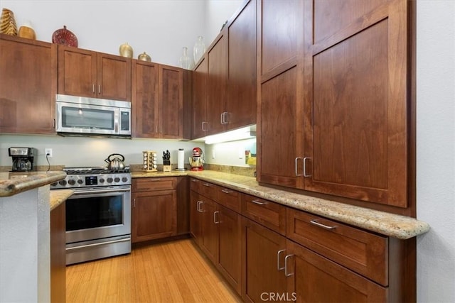 kitchen with stainless steel appliances, light stone counters, and light wood-type flooring