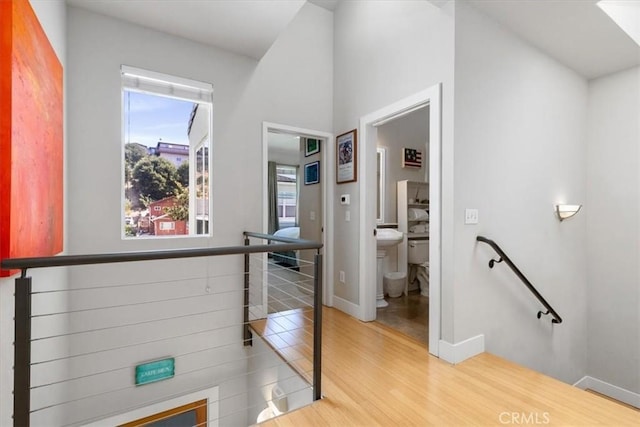 hall featuring baseboards, wood finished floors, and an upstairs landing