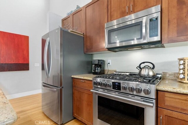 kitchen with light hardwood / wood-style flooring, light stone countertops, and stainless steel appliances