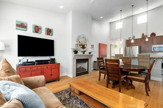 living room with baseboards, a high ceiling, a fireplace, and light wood-style floors