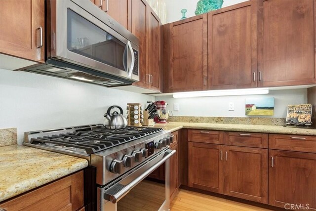 kitchen with light hardwood / wood-style floors, stainless steel appliances, and light stone countertops