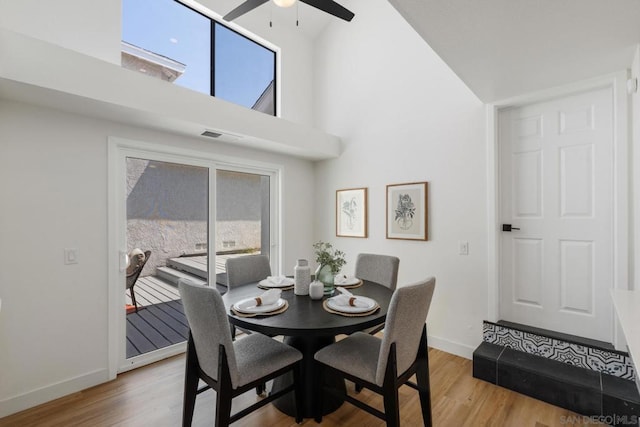 dining area featuring a towering ceiling, wood-type flooring, and ceiling fan