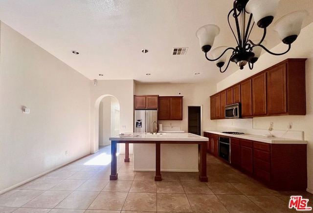 kitchen featuring appliances with stainless steel finishes, a center island with sink, light tile patterned floors, and a chandelier