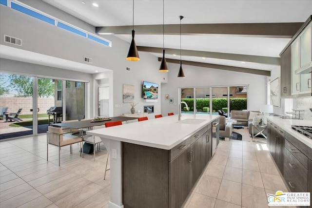 kitchen featuring sink, an island with sink, beamed ceiling, decorative light fixtures, and dark brown cabinetry