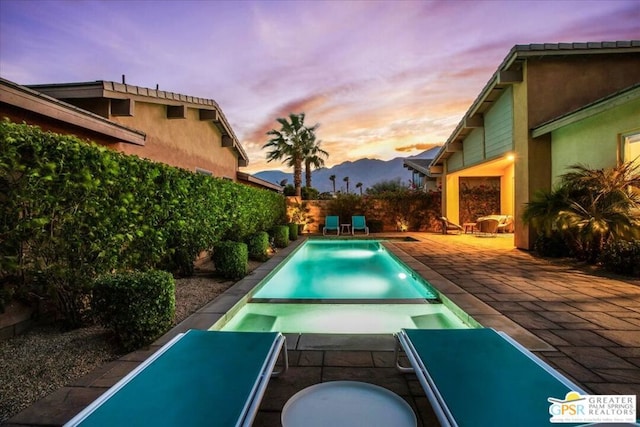 pool at dusk featuring a mountain view and a patio