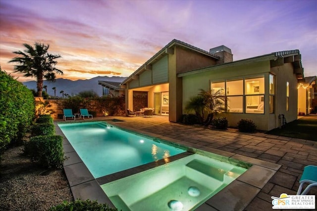 pool at dusk featuring an in ground hot tub and a patio