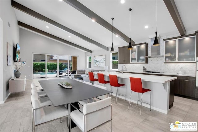 kitchen featuring black gas cooktop, wall chimney range hood, vaulted ceiling with beams, tasteful backsplash, and a large island