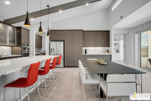 kitchen featuring decorative backsplash, appliances with stainless steel finishes, dark brown cabinetry, and an island with sink