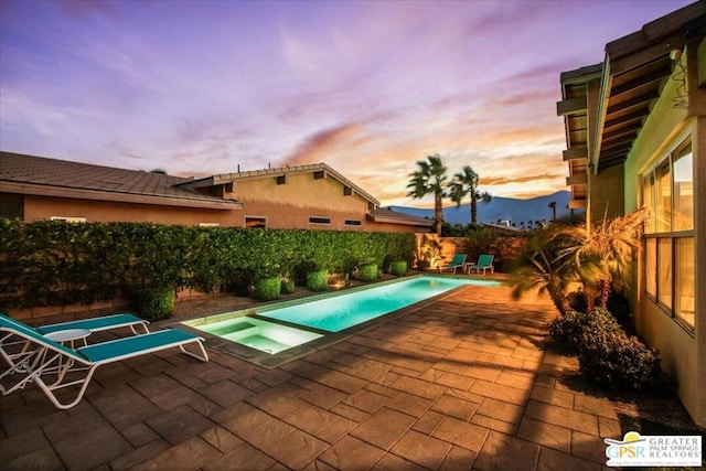 pool at dusk featuring an in ground hot tub and a patio