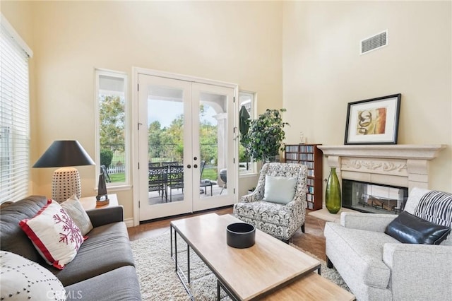 living room with french doors, a towering ceiling, a healthy amount of sunlight, and light hardwood / wood-style floors