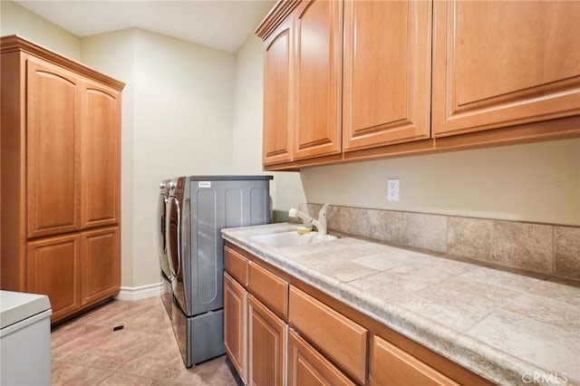 clothes washing area with washer and dryer, light tile patterned flooring, cabinets, and sink