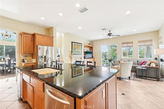 kitchen with sink, dark stone countertops, a kitchen island with sink, ceiling fan with notable chandelier, and appliances with stainless steel finishes