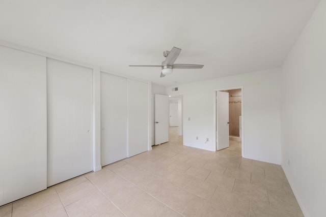 unfurnished bedroom featuring light tile patterned floors, ceiling fan, and multiple closets