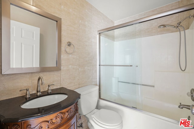 full bathroom with tile walls, combined bath / shower with glass door, vanity, and toilet