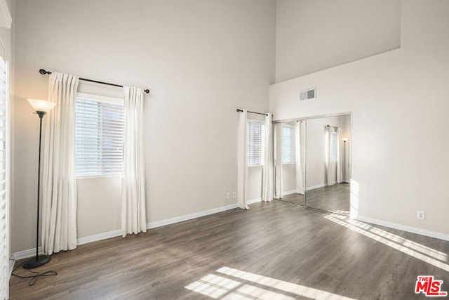 empty room featuring hardwood / wood-style flooring, a towering ceiling, and a healthy amount of sunlight