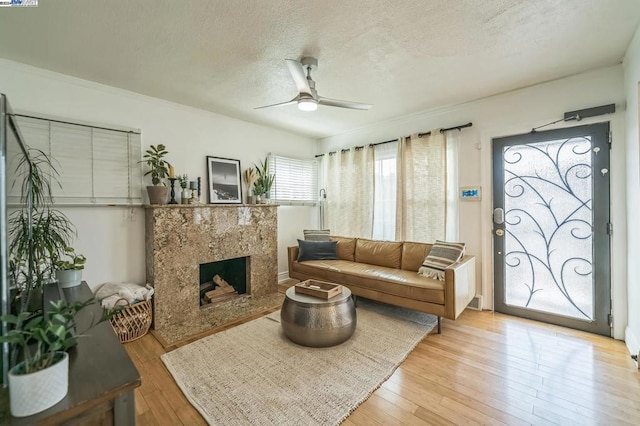 living room featuring light hardwood / wood-style flooring, a textured ceiling, ceiling fan, and a high end fireplace