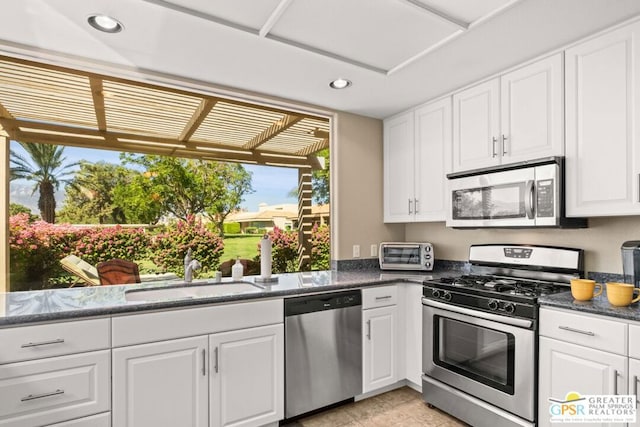 kitchen with white cabinets, stainless steel appliances, sink, and dark stone counters