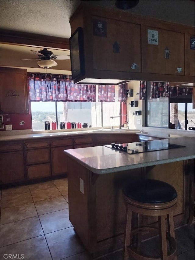 kitchen featuring a kitchen bar, kitchen peninsula, a textured ceiling, ceiling fan, and light tile patterned floors