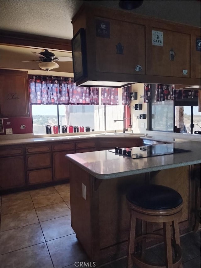 kitchen with ceiling fan, kitchen peninsula, a textured ceiling, a breakfast bar area, and light tile patterned flooring